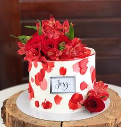 a red and white cake with flowers on it sitting on top of a tree stump