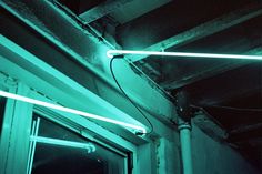 two green lights are hanging from the ceiling above a window in a dark room with exposed pipes