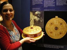 a woman holding up a decorative object in front of a wall with pictures on it