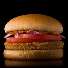 a chicken sandwich with tomato, onion and lettuce on a black background in the dark