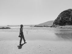 a woman walking on the beach with her feet in the sand and an island in the background