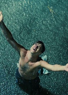 a shirtless man holding an umbrella and throwing it in the air while standing under water