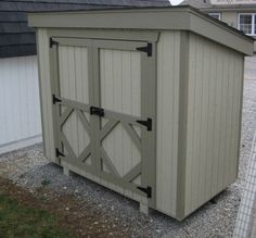 a small storage shed with the door open on gravel ground in front of a house