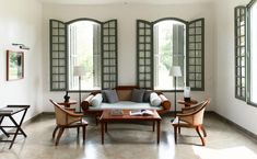 a living room filled with lots of furniture next to two large windows and tables in front of them