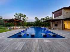 an outdoor swimming pool with lounge chairs and lights on the side, in front of a house