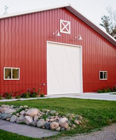 a large red barn with a white door and windows on the side, grass in front of it