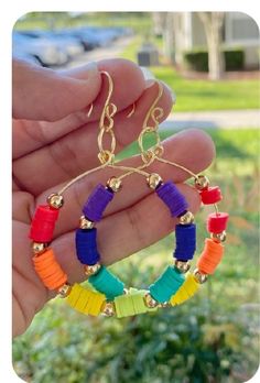 a person holding up a pair of colorful hoop earrings with gold beads on each end