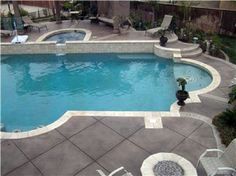 an empty swimming pool surrounded by lawn chairs and loungers in a backyard area with concrete pavers