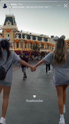 two young women holding hands in front of a large building with people walking around it