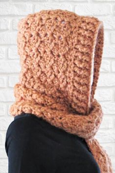 a person wearing a crocheted scarf with a hood on their head is shown in front of a brick wall