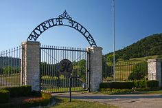 an iron gate with a sign that says mary's gardens on it and a flag flying in the background