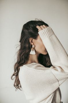 a woman with her hand on her head and wearing white sweater, jeans and earrings