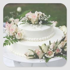 a wedding cake decorated with flowers and greenery sits on a white tablecloth outdoors