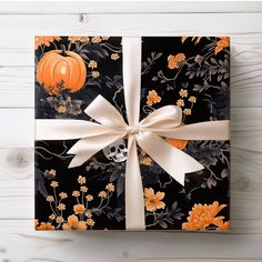 a halloween gift wrapped in black paper with white ribbon and pumpkins on the side