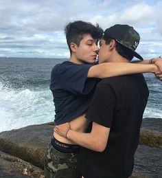 two young men embracing each other near the ocean with waves crashing in the back ground