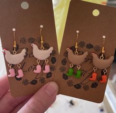 two small bird earrings are being held in front of a card with the same design on it