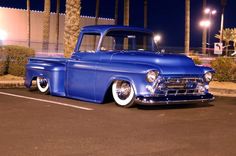 an old blue pickup truck parked in a parking lot at night with palm trees behind it