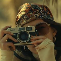 a woman taking a photo with her camera in front of her face and wearing a bandana