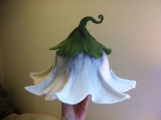 a hand holding a white and blue flower with green leaves on it's head