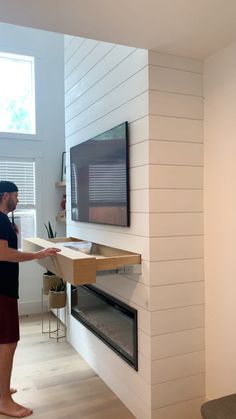 a man standing in front of a flat screen tv mounted on a wall next to a fireplace