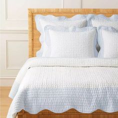 a bed with white linens and pillows on it in front of a wooden headboard