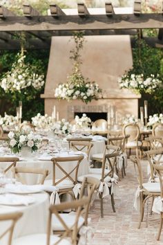 tables and chairs are set up in front of an outdoor fireplace with white flowers on it