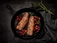 two fish fillets in a skillet with grapes and asparagus on the side