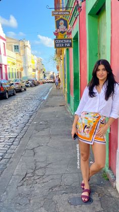 a woman standing on the side of a street next to a building with colorful walls