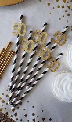 black and white striped straws with gold glitter numbers on them next to cupcakes