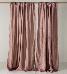 two pink curtains hanging on a wooden rail in front of a white wall and floor