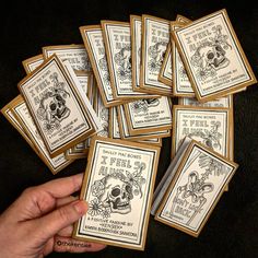 a person holding up some cards with skulls and flowers on them in front of a black background