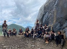 a group of people sitting next to each other on top of a rocky hill with mountains in the background