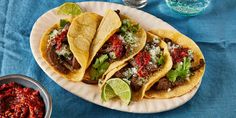 three tacos on a paper plate with salsa and lime wedges next to it