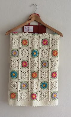 a white crocheted blanket hanging on a wooden hanger next to a wall