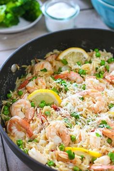 a skillet filled with shrimp, rice and lemon wedges on a wooden table