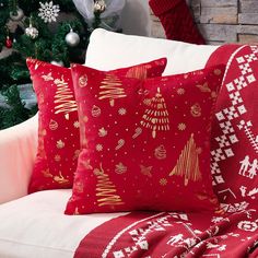 two red christmas pillows sitting on top of a white couch next to a christmas tree