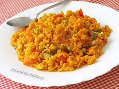 a white plate topped with rice covered in peas and carrots next to a spoon