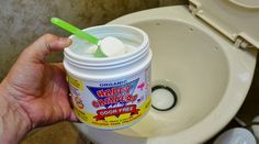 a person holding a cup of yogurt in front of a toilet with the lid up