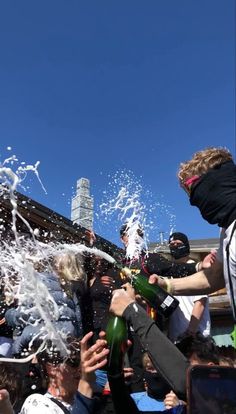 a group of people standing around each other with water pouring out of their bottles in the air