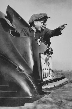 an old photo of a man sitting in the back of a car pointing at something