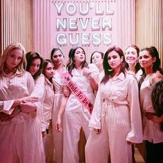 a group of women standing next to each other in front of a pink sign that says you'll never guess