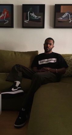 a man sitting on top of a couch in front of three framed pictures above him