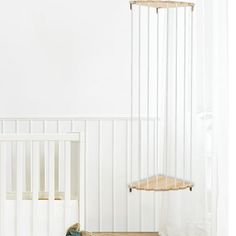 a baby crib in a white room next to a wooden shelf with clothes hanging from it