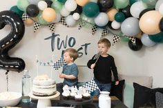 two boys standing in front of a table with cake and cupcakes on it