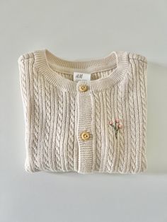 This sweet little sweater is machine knit (not handmade) but is hand embroidered by me. It is 100% organic cotton and available in size 6 months or 12 months. A beautiful creamy beige cable knit and hand embroidered with a delicate pink floral branch. Brand new.  Made in a smoke free and pet free environment. Embroidered Cream Cotton Sweater, Cream Cotton Embroidered Sweater, Cream Embroidered Cotton Sweater, Cute Cream Cotton Sweater, Beige Embroidered Cotton Cardigan, Cute Embroidered Cotton Cardigan, Cream Knit Sweater With Floral Embroidery, Beige Cotton Cable Knit Sweater, Cute Cotton Cable Knit Sweater