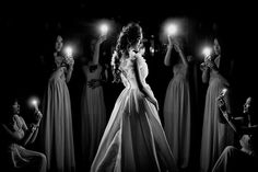 a woman standing in front of a group of women holding lit candles up to her face