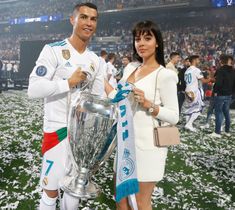 a man and woman standing next to each other holding a soccer trophy in front of a crowd