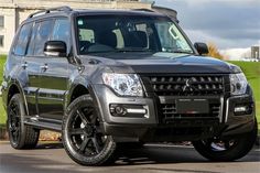 a black suv is parked in front of a building with grass and trees behind it