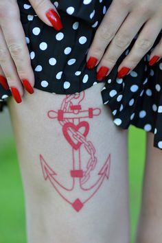 a woman with red nail polish holding onto an anchor tattoo on her thigh, while wearing polka dots