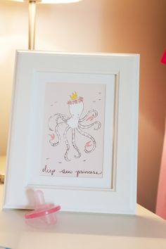 a pink pacifier sitting on top of a white table next to a framed print